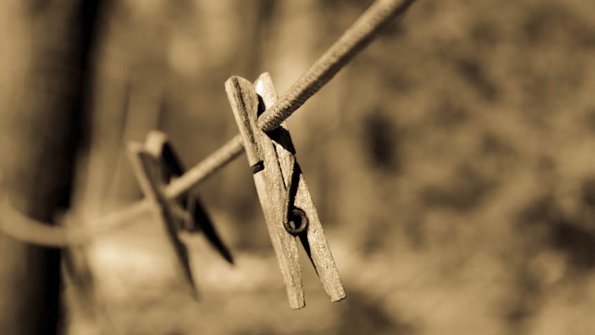A sepia-toned image featuring a wooden clothespin on a clothesline outdoors.