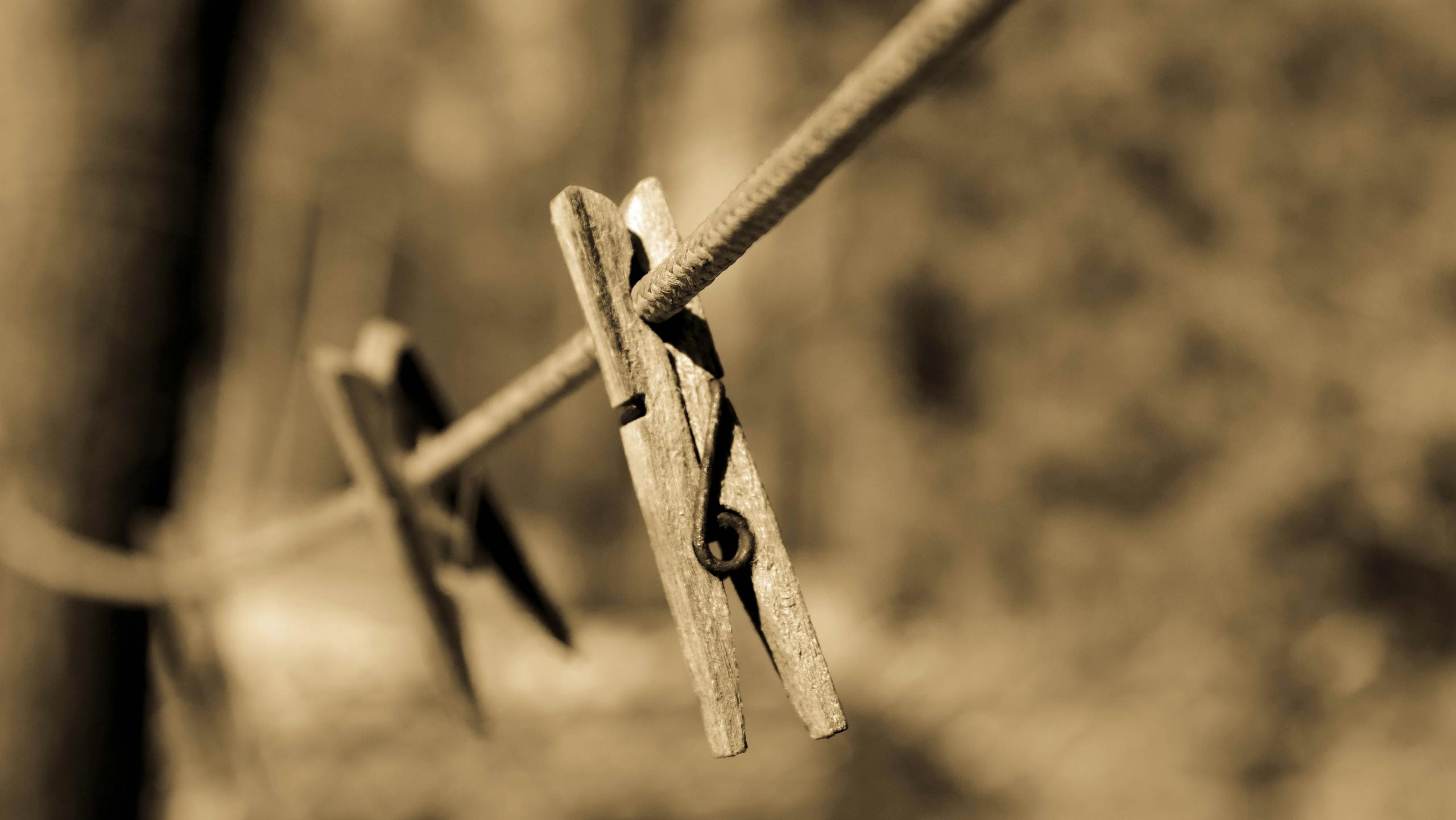 A sepia-toned image featuring a wooden clothespin on a clothesline outdoors.