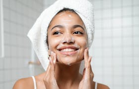 Smiling woman with face wash in a bathroom, embracing self-care and fresh skin.