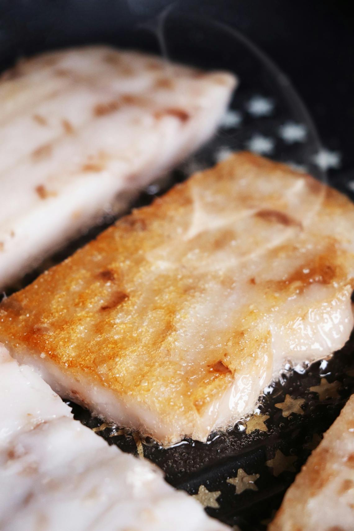 Close-up of sizzling golden-brown fish fillets frying in a pan.