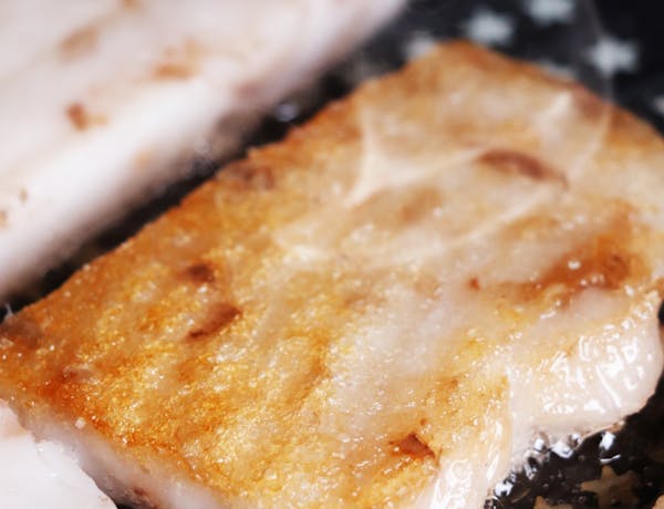 Close-up of sizzling golden-brown fish fillets frying in a pan.