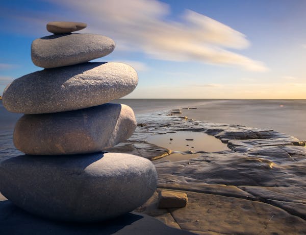 A serene stack of stones on the rocky seashore during a peaceful sunrise, embodying balance and zen.