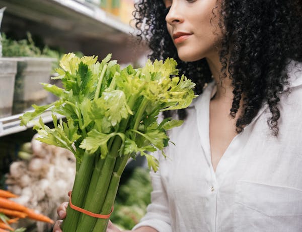 A woman examines a fresh bunch of celery in a produce aisle at the grocery store.