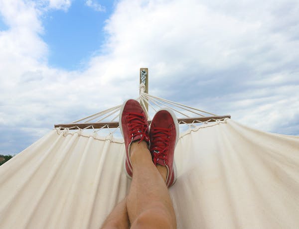 Feet resting on a hammock with red sneakers, epitomizing summer relaxation and leisure outdoors.